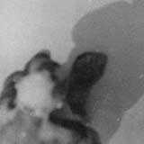 Fotografia em preto e branco, tirada do alto. Nota-se um homem sentado no chão, abraçando as pernas. Destaca-se também a sombra dele projetada à frente.