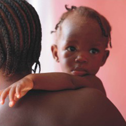 Nesta foto em close, mulher negra de costas e bebê negro de frente para a câmera. Nota-se que a mulher tem cabelos curtos e usa penteado estilo rastafári e segura no colo a criança. Esta, olha para outra direção que não a do fotógrafo. Percebe-se ainda uma feição séria e curiosa em seu rosto infantil.