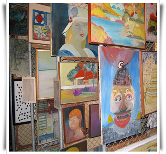 Fotografia de vários quadros fixados em suportes metálicos verticais. Alguns quadros são coloridos e outros são em preto e branco. Retratam paisagens, objetos e figuras humanas.