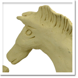 Foto colorida de uma escultura em tom claro. A obra exibe dois animais ligados pela mesma massa que os compõe. Um deles, à direita, é identificado como um cavalo que está de frente e com o focinho bem próximo ao segundo animal, não identificado.