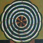 Mandala que concentra círculos, uns dentro dos outros nas cores branca, azul, verde e preta. O círculo maior e, portanto, mais externo, é contornado por uma linha preta com relevos. O centro possui um ponto amarelo, envolto por um círculo que se divide em doze pedaços simétricos e intercalados, nas cores preta e vermelha. Do centro até os limites da mandala, linhas finas e vermelhas cortam os círculos em curva e em pedaços iguais. A base da pintura é preta nas laterais inferiores e vermelha no meio. O fundo foi colorido em tons de amarelo, marrom e verde. 