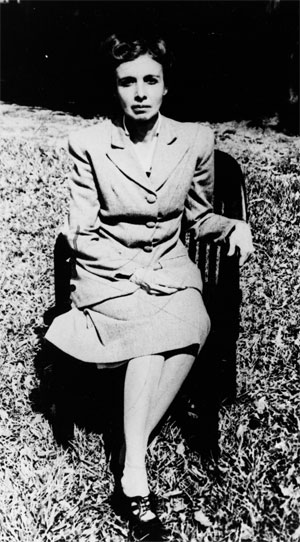 A fotografia, em preto e branco, mostra a psiquiatra Nise da Silveira ainda jovem, com uma expressão facial séria, sentada em uma cadeira sobre a grama. Ela está com os cabelos presos, veste um tailleur em cor clara e calça sapatos escuros. A mão esquerda está apoiada sobre a lateral da cadeira e a mão direita, sobre o colo. A fotografia, em preto e branco, mostra a psiquiatra Nise da Silveira ainda jovem, com uma expressão facial séria, sentada em uma cadeira sobre a grama. Ela está com os cabelos presos, veste um tailleur em cor clara e calça sapatos escuros. A mão esquerda está apoiada sobre a lateral da cadeira e a mão direita, sobre o colo.