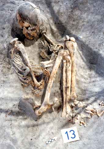 A fotografia mostra um esqueleto parcialmente enterrado com os joelhos recolhidos.