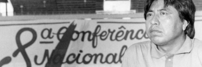 Índio à direita. No fundo (completando boa parte da imagem) o anúncio da oitava conferência nacional de saúde