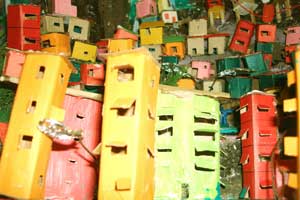 Esta foto em close revela espécie de maquete onde, imediatamente, se reconhece uma favela ou comunidade. Há casas e prédios coloridos, construídos desordenadamente, acompanhando o contorno do morro que ocupam.