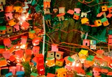 Foto revela maquete na qual se reconhece fração de uma comunidade ou favela que cresceu sobre um morro. As pequenas casas coloridas e prédios foram erguidos sem planejamento, ocupando os contornos do monte. Notam-se muitos fios, também desordenados, representando as ligações caseiras que levam energia elétrica às moradias.