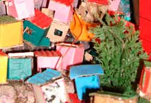 Esta foto em close revela espécie de maquete onde, imediatamente, se reconhece uma favela ou comunidade. Há casas coloridas, construídas desordenadamente, acompanhando o contorno do morro que ocupam.